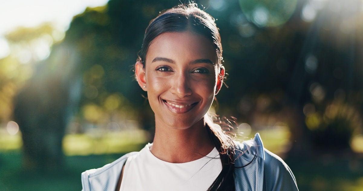 Person standing outdoors in a park, wearing athletic clothing in soft sunlight.