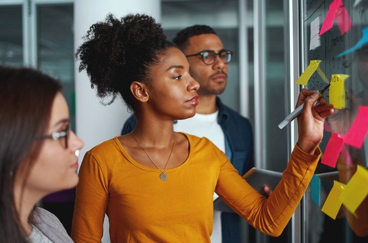 Executives looking at businesswoman writing on adhesive notes stuck over glass