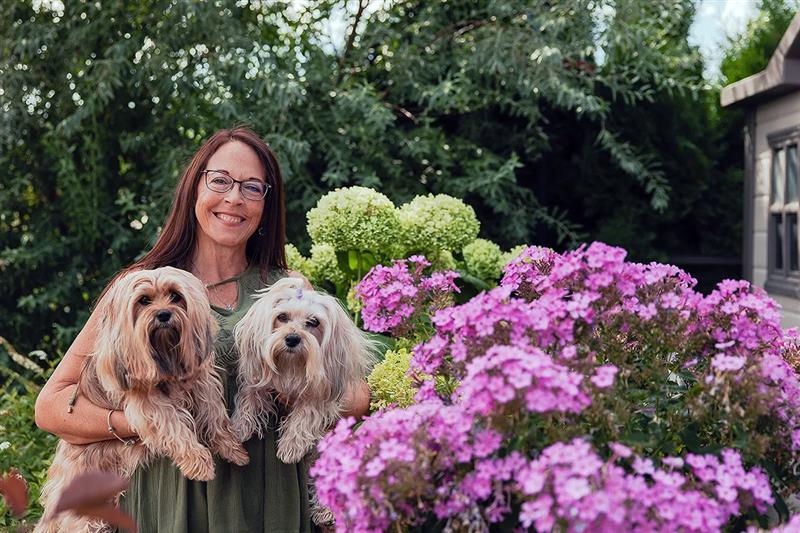 Cancer survivor hugging two dogs and smiling in a floral landscape