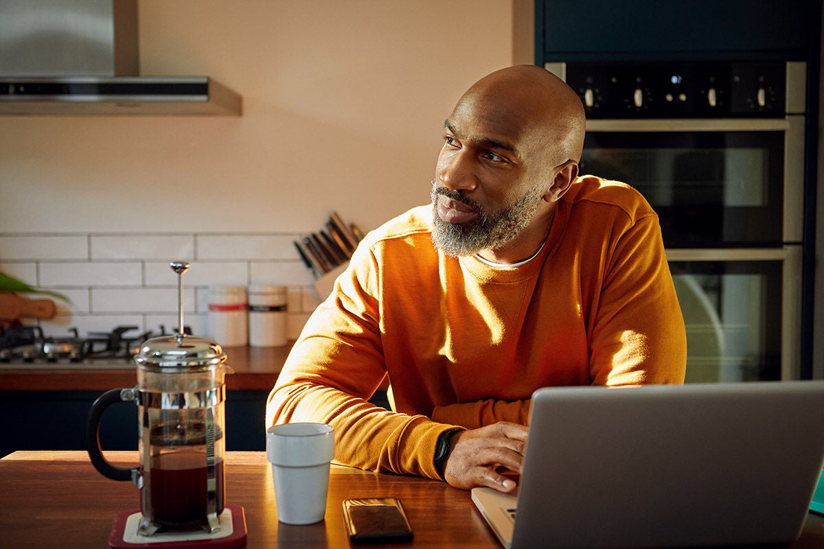 Individual managing personal finances and online banking on laptop at home kitchen
