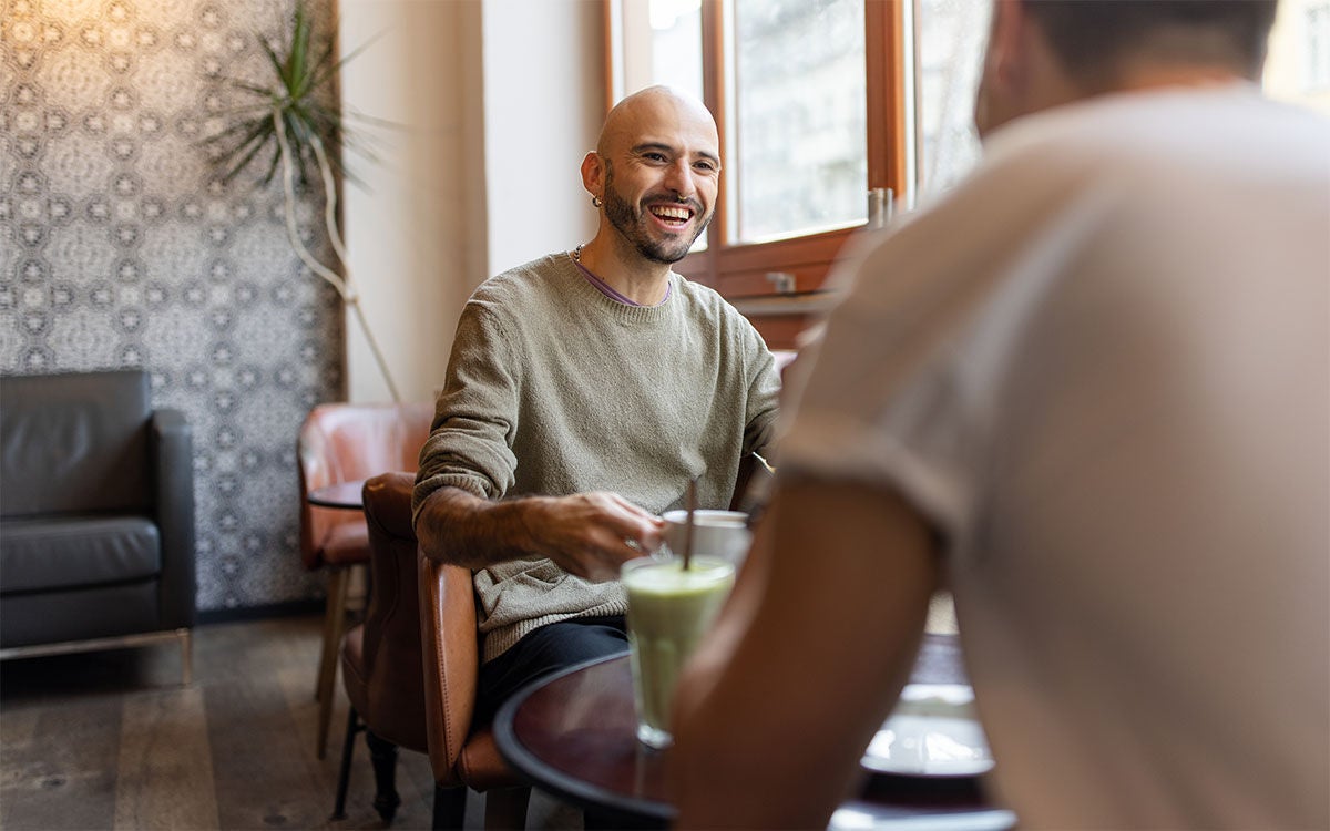 Man in light sweater having coffee with a friend at a coffee shop.