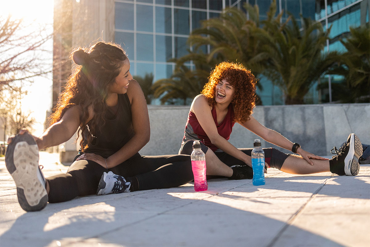 Two friends stretching in exercise gear while seated on the ground