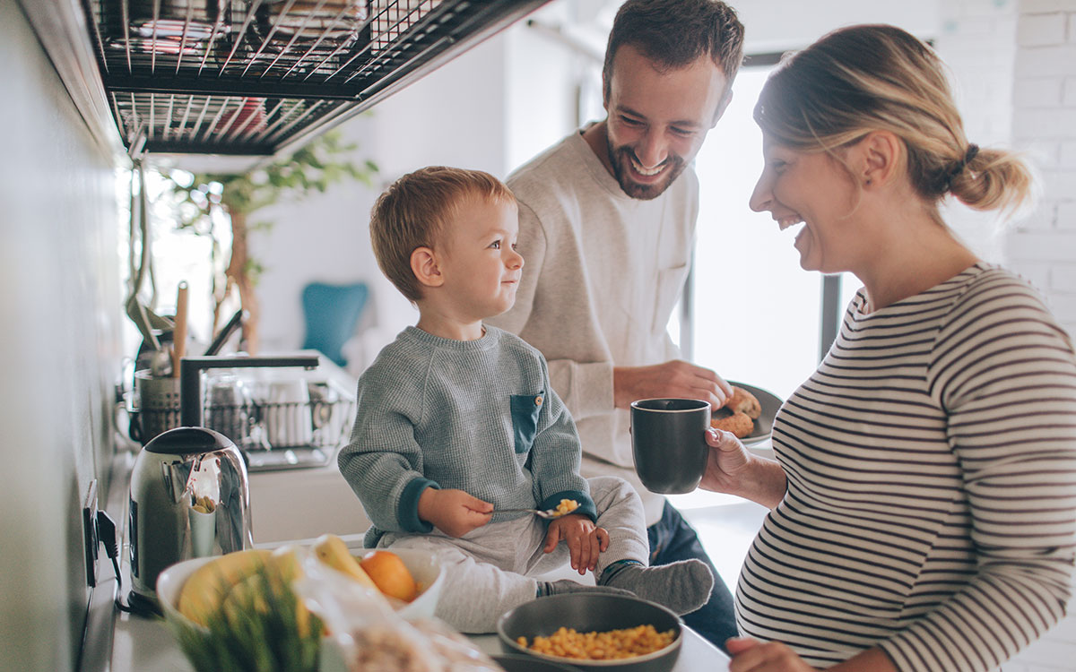 Young family of 3 laughing in the kitchen having some food