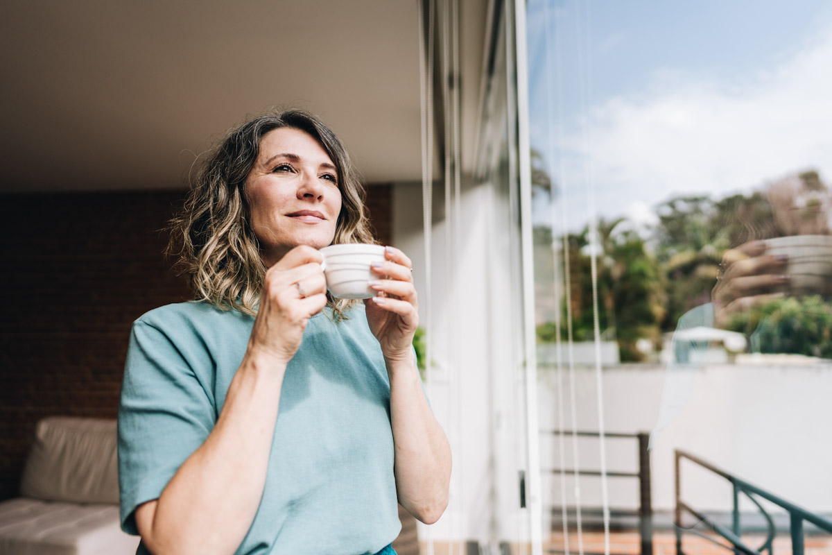 A woman holding a mug while staring out her home
